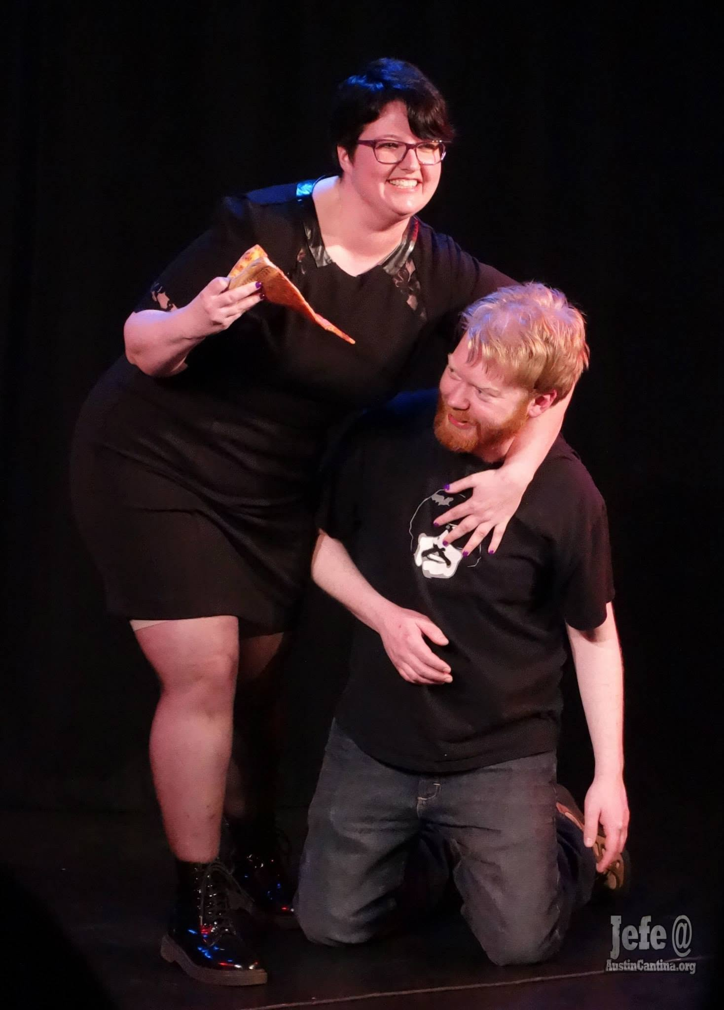 Violet holding an oversized pizza slice during a comedy performance
